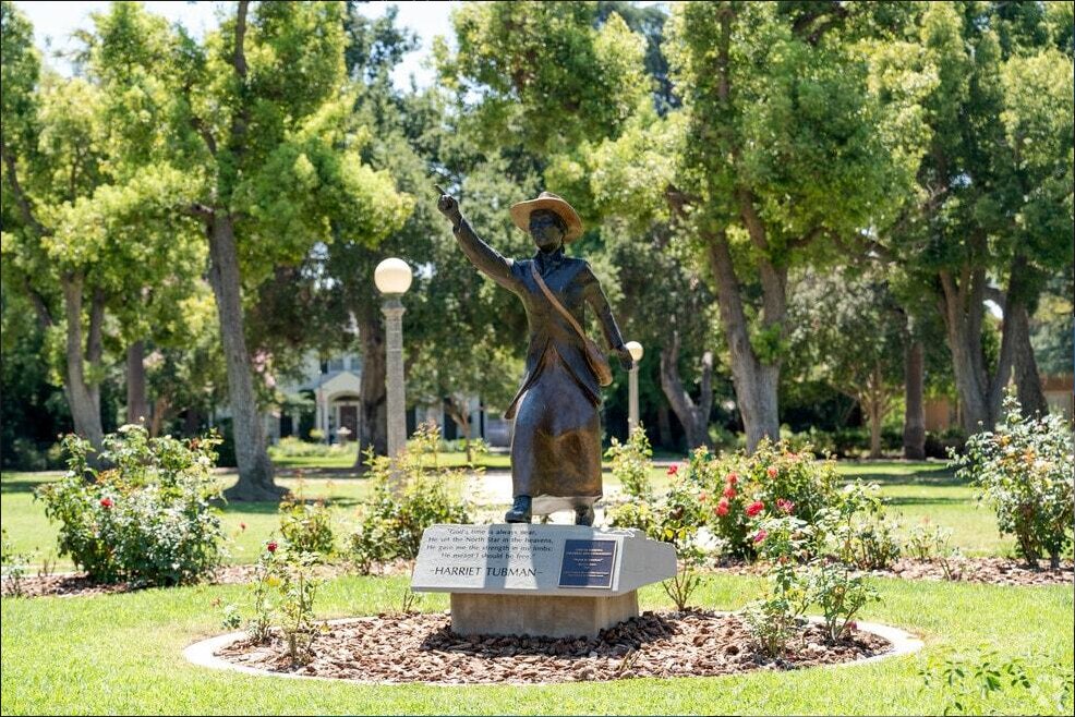 Bronze Harriet Tubman statue pointing skyward among trees and rose bushes in Lincoln Park, Pomona, on a stone base inscribed with her words