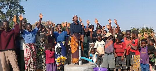 Villagers in Tanzania celebrating with raised hands around a new clean-water well pump